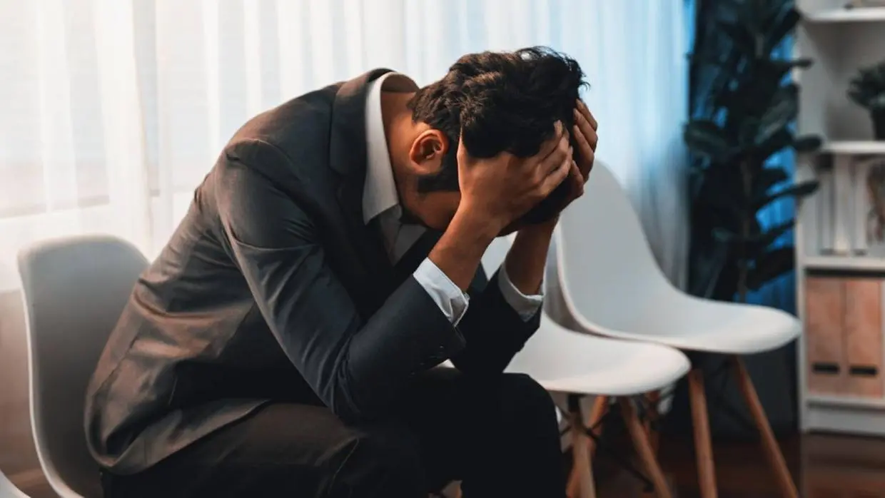 Imagem mostra homem em ambiente de trabalho com a cabeça baixa.