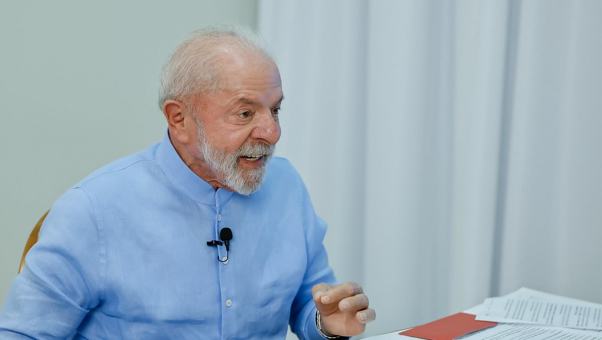 Lula de camisa azul em uma entrevista. Ele aparece usando um microfone de lapela