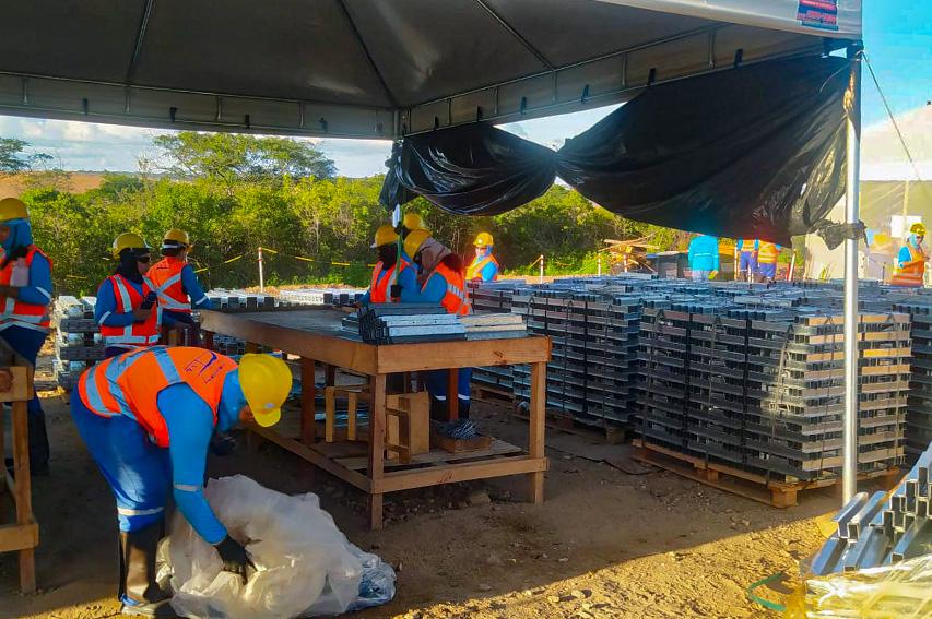 Trabalhadores de uniforme azul e colete laranja trabalham sob tenda na instalação de paineis de energia solar em Icó