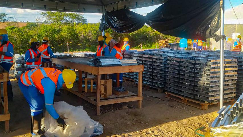 Trabalhadores de uniforme azul e colete laranja trabalham sob tenda na instalação de paineis de energia solar em Icó