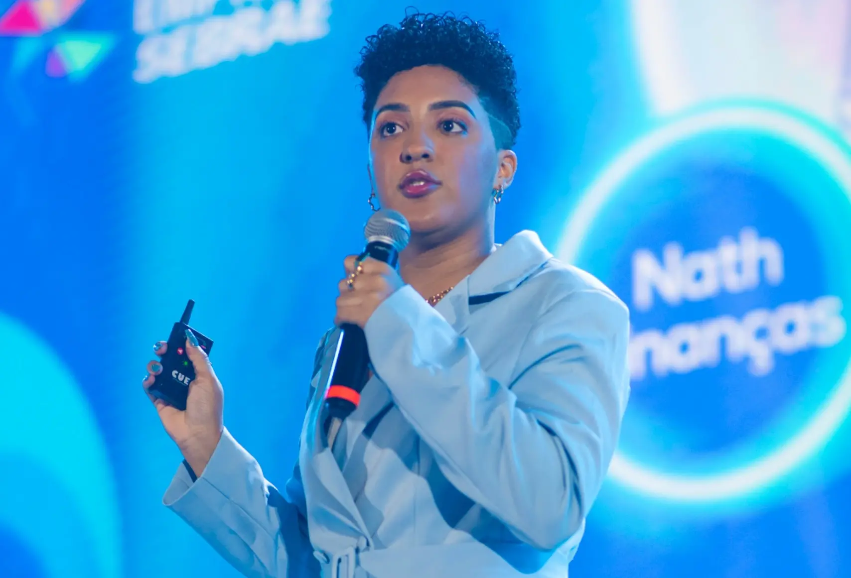 Nath Finanças, uma mulher negra, fala ao microfone durante palestra sobre educação financeira.
