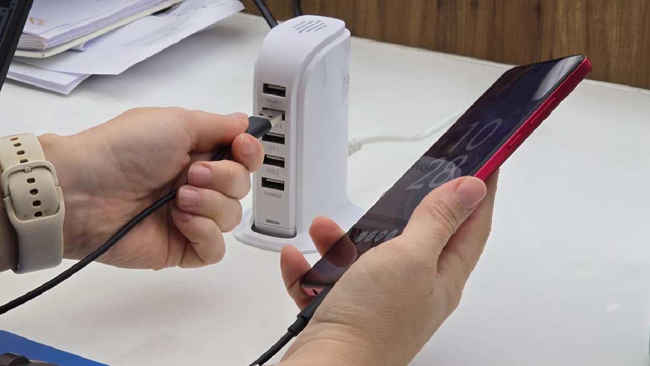 Uma mulher segura um cabo USB ligado a um celular que será carregado em um base de cabos USBs