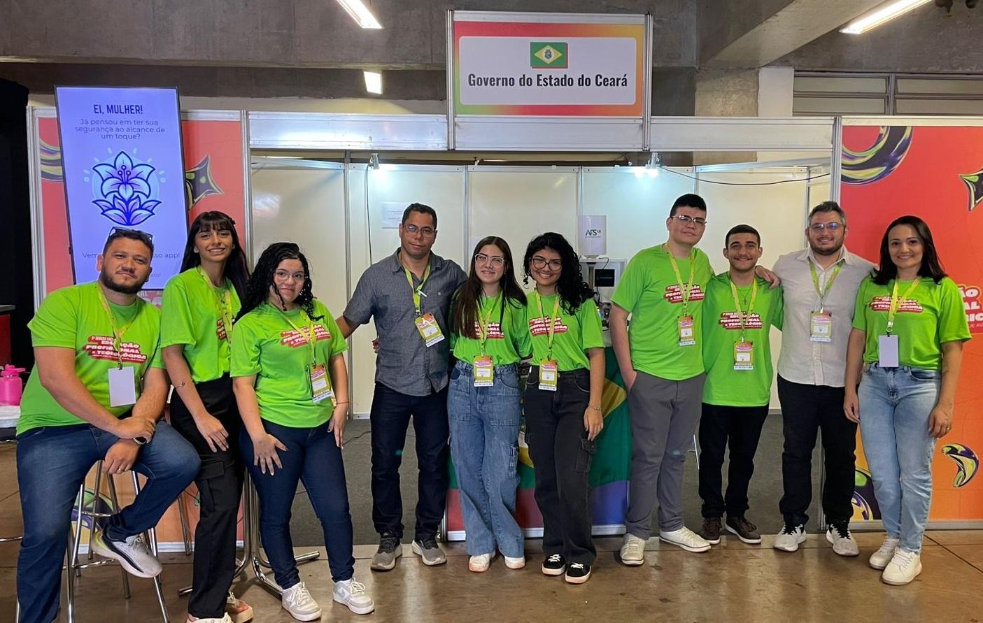 Foto com 10 pessoas com crachás, sendo seis alunos e quatro professores, posando para foto em frente a estande de feira científica representando o Estado do Ceará. Os alunos usam blusas verdes do evento.