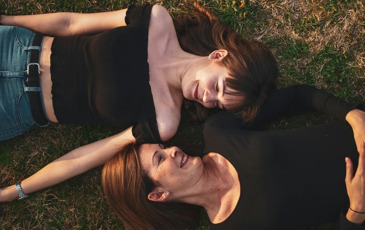 Duas mulheres, uma mais velha e uma mais nova, deitadas no chão e olhando uma para a outra.