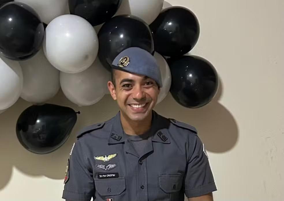 Imagem do PM morto durante romaria para Aparecida, vestindo uniforme e sorrindo, com balões brancos e pretos atrás.