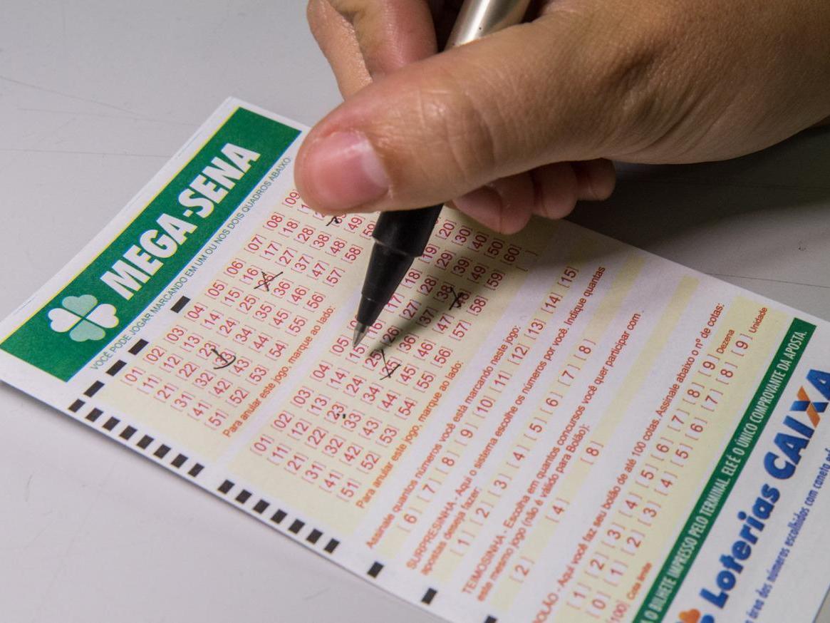 Pessoa preenchendo com caneta o volante do concurso da Mega-Sena, da Caixa