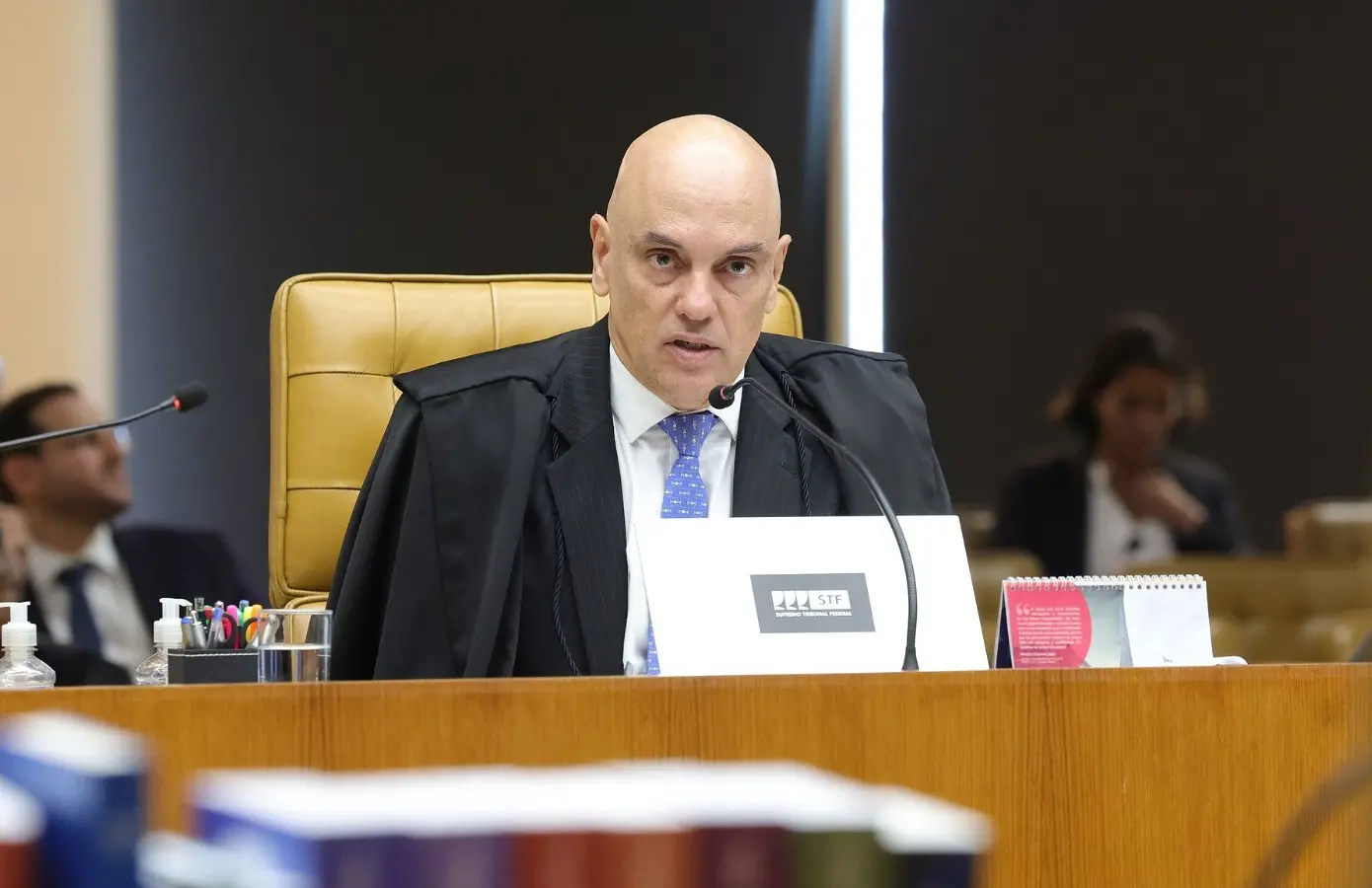 Alexandre de Moraes discursa em plenário no STF. Ele é um homem branco e careca, de meia idade, e usa um terno preto com camisa social branca e gravata azul.