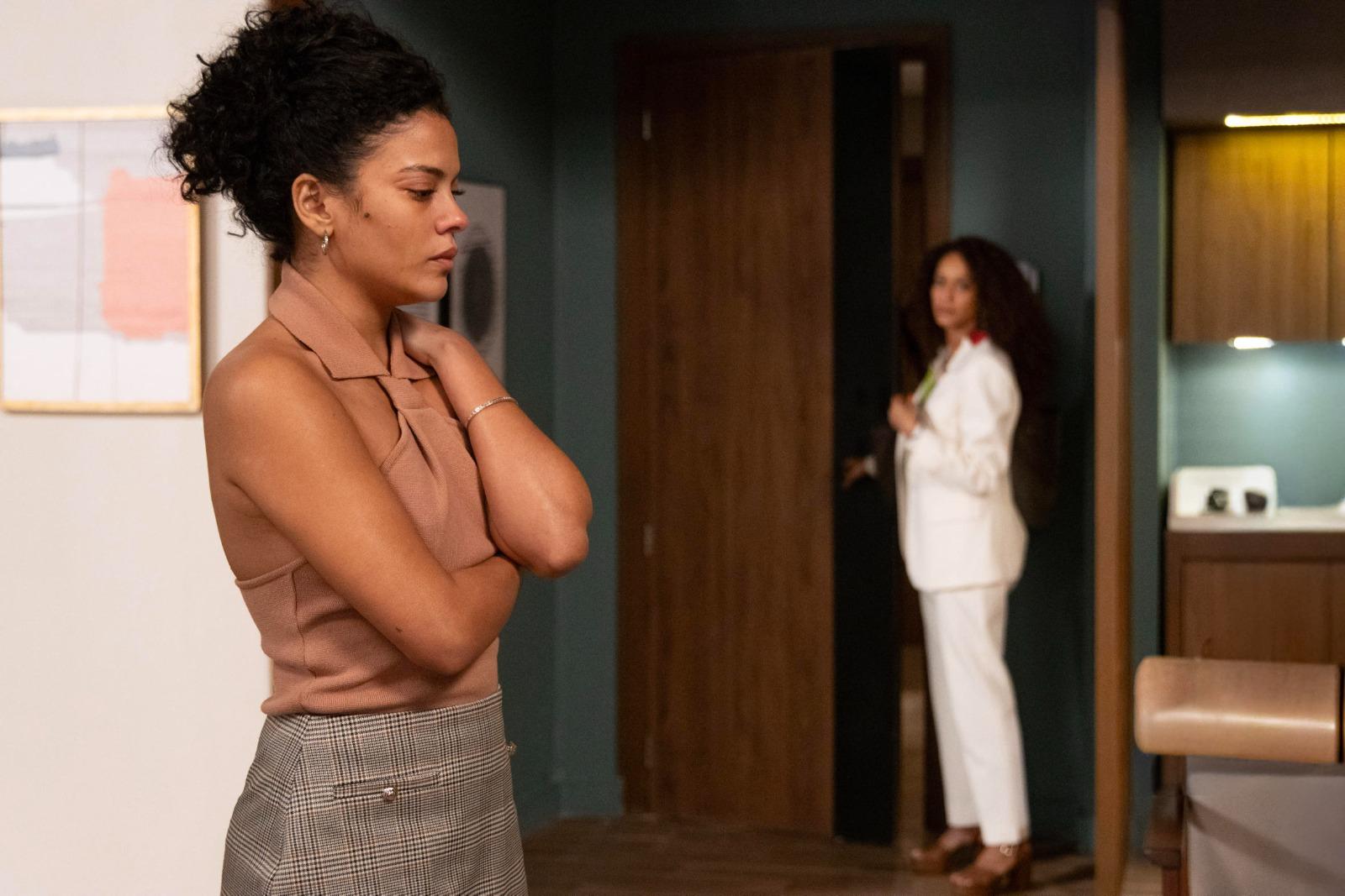 Cena de Vale Tudo, onde Raquel (Tais Araujo) se encontra ao fundo na porta do apartamento de Maria de Fátima (Bela Campos), que se mostra abalada.