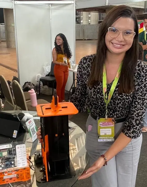 Aluna do IFCE com crachá de feira científica e blusa estampada mostra mini elevador construído com impressão 3D e micro sensores.