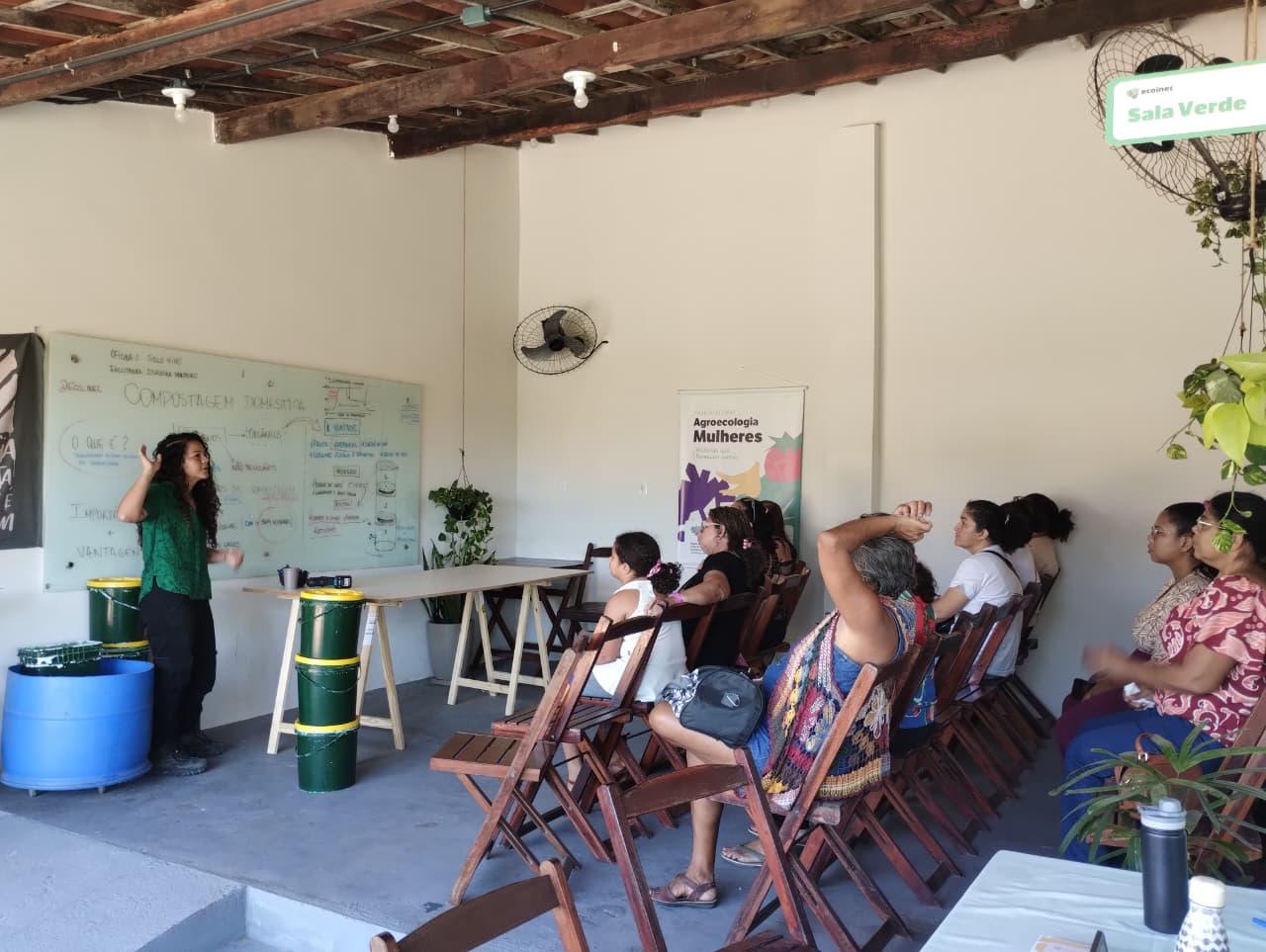 Imagem mostra uma professora ensinando um grupo de mulheres durante o curso.
