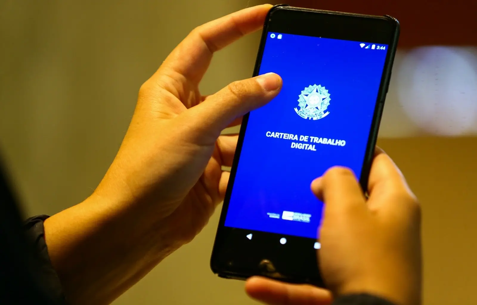Mãos seguram celular aberto no aplicativo Carteira de Trabalho Digital.
