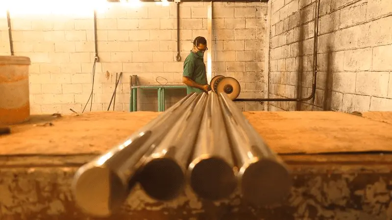 Trabalhador manuseia barras de ferro fundido em oficina industrial, representando o setor metalúrgico e a produção de peças no Ceará.