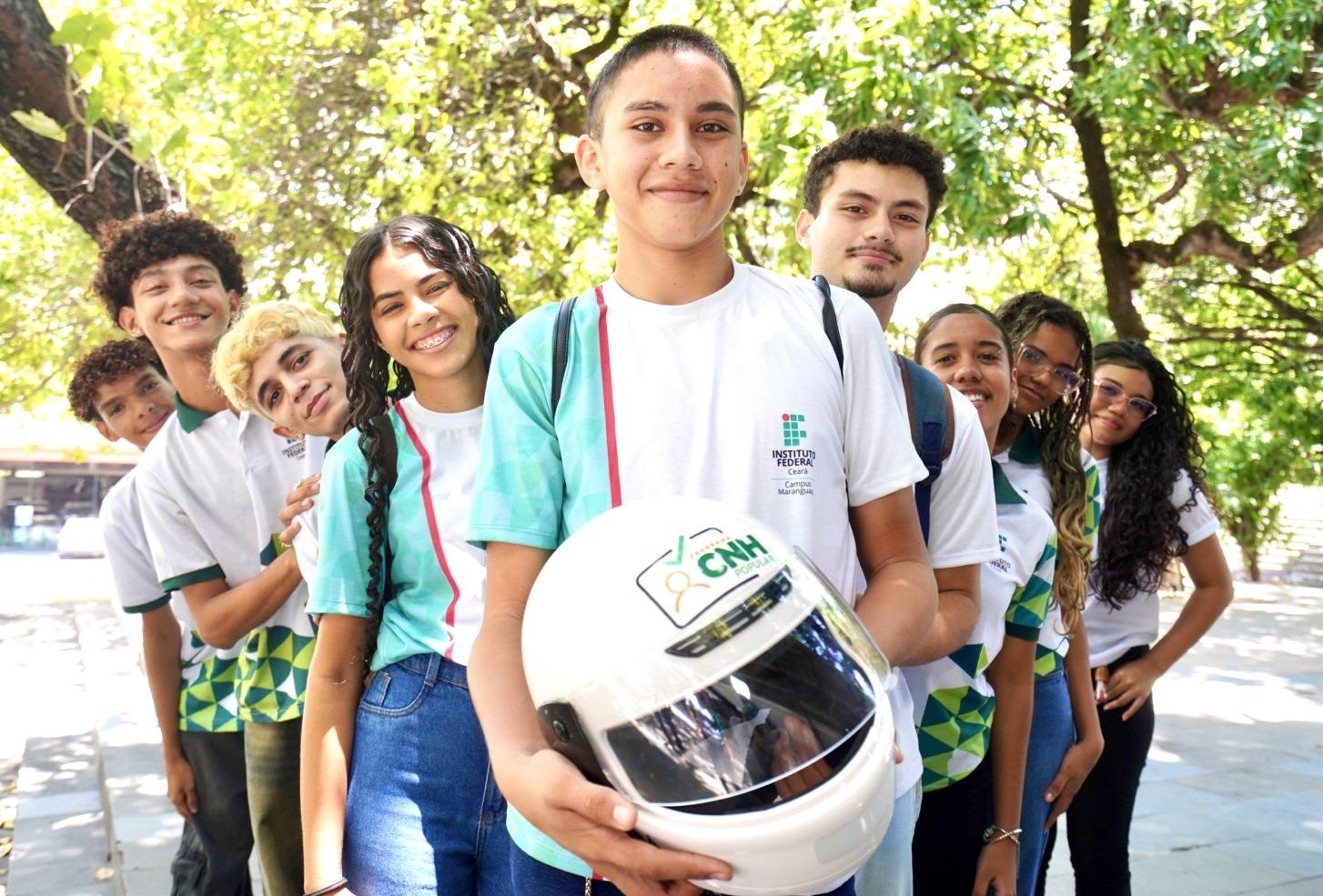 Estudantes da rede pública cearense posam para foto em parque estadual. O estudante do meio da foto segura um capacete branco de motociclista.
