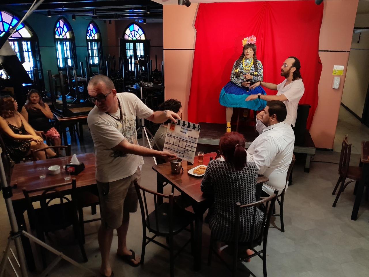 Imagem dos bastidores da gravação da comédia cearense 'Filosofia de Boteco', mostrando um local como um bar com clientes em mesas e um palco.