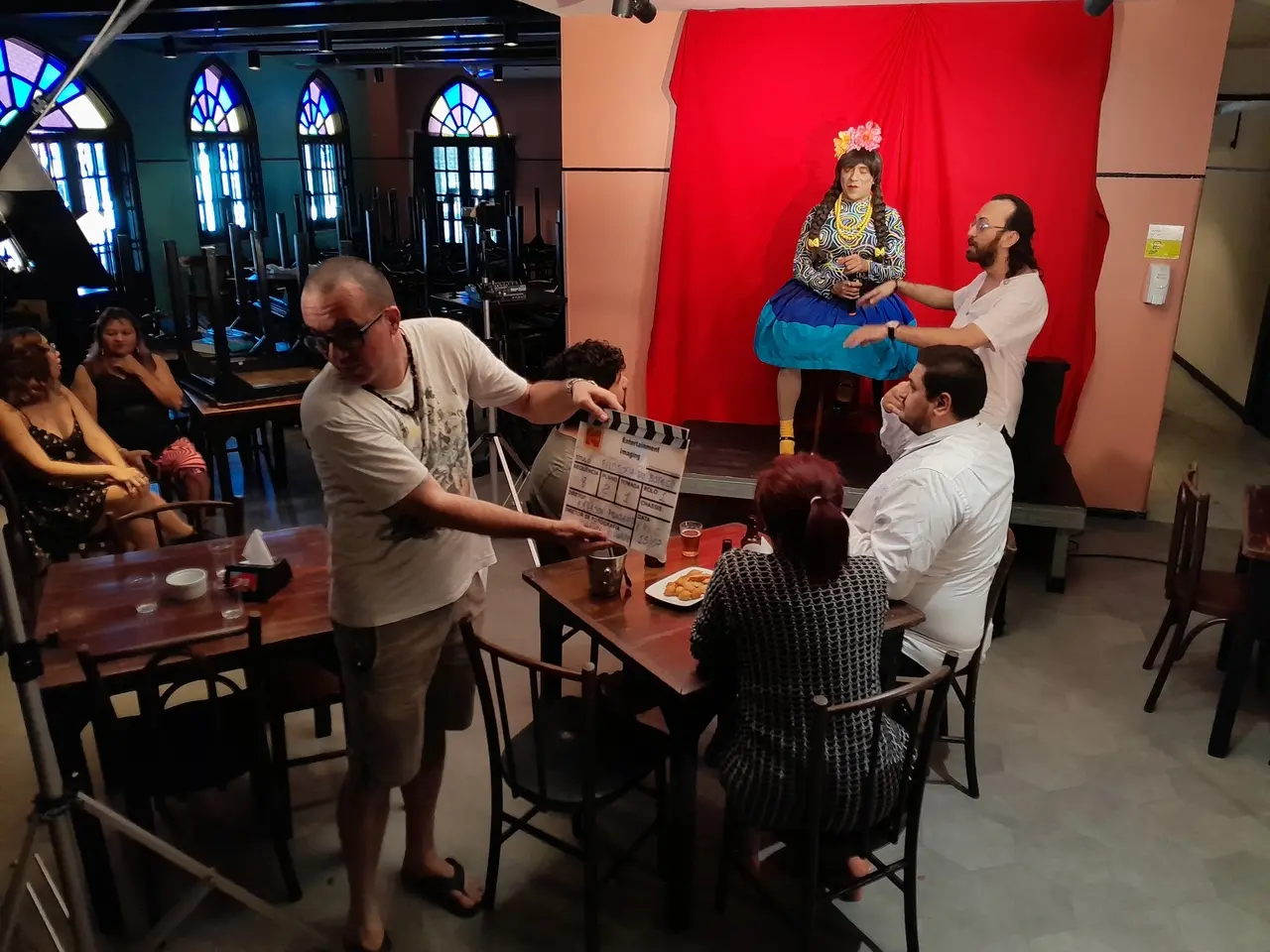 Imagem dos bastidores da gravação da comédia cearense 'Filosofia de Boteco', mostrando um local como um bar com clientes em mesas e um palco.
