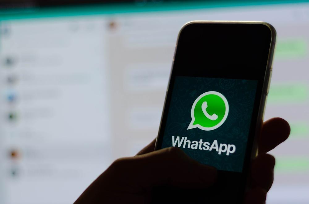 Sombra de mão segura celular aberto no aplicativo do WhatsApp em frente ao WhatsApp Web.