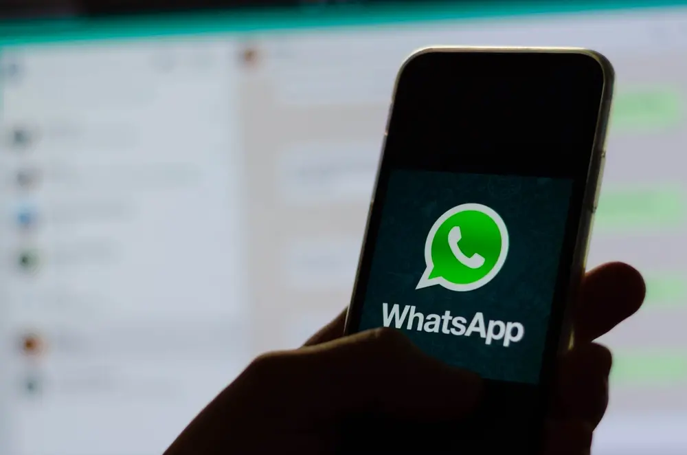 Sombra de mão segura celular aberto no aplicativo do WhatsApp em frente ao WhatsApp Web.
