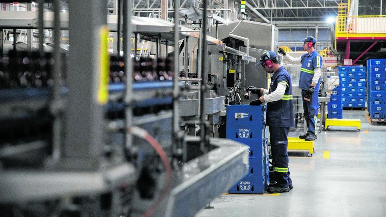 Trabalhadores atuam em linha de produção industrial com garrafas e caixas empilhadas, representando a atividade fabril no Ceará.