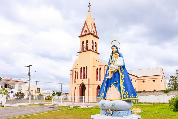 Igreja Matriz de Nossa Senhora da Conceição com estátua de Maria e o Menino Jesus em Capistrano, no interior do Ceará, sob céu nublado.
