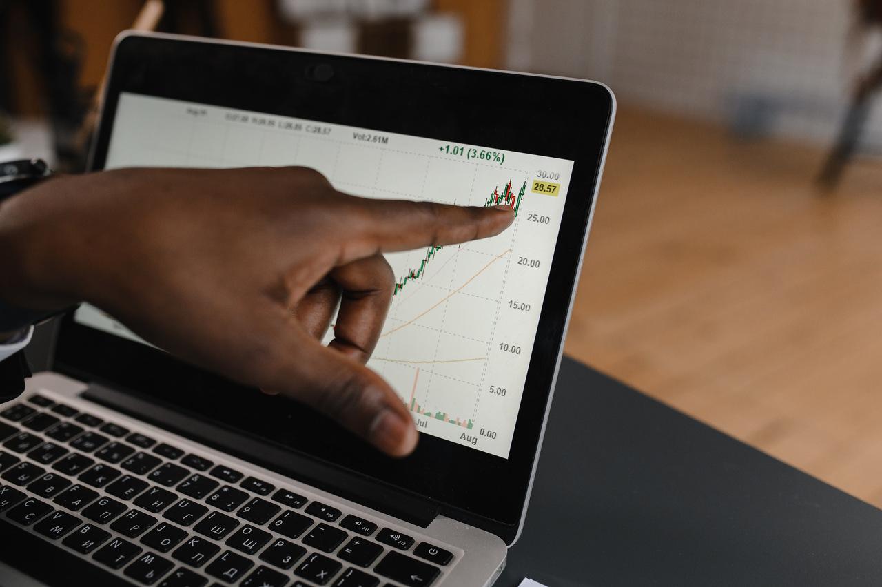 Mão de pessoa preta apontando para gráficos financeiros em um laptop.