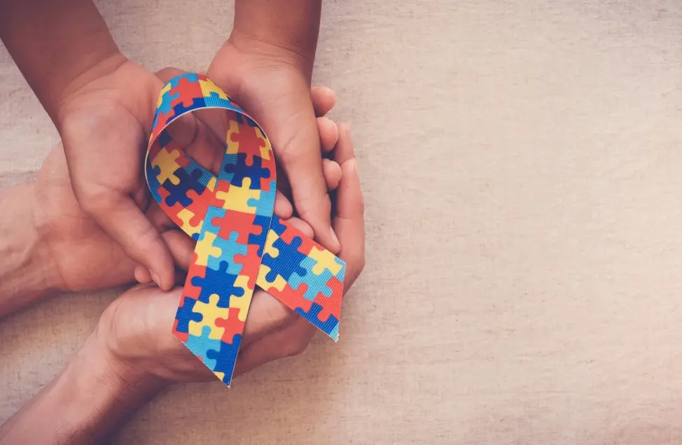 Mãos segurando fita quebra-cabeça para o Dia Mundial da Consciência do Autismo.