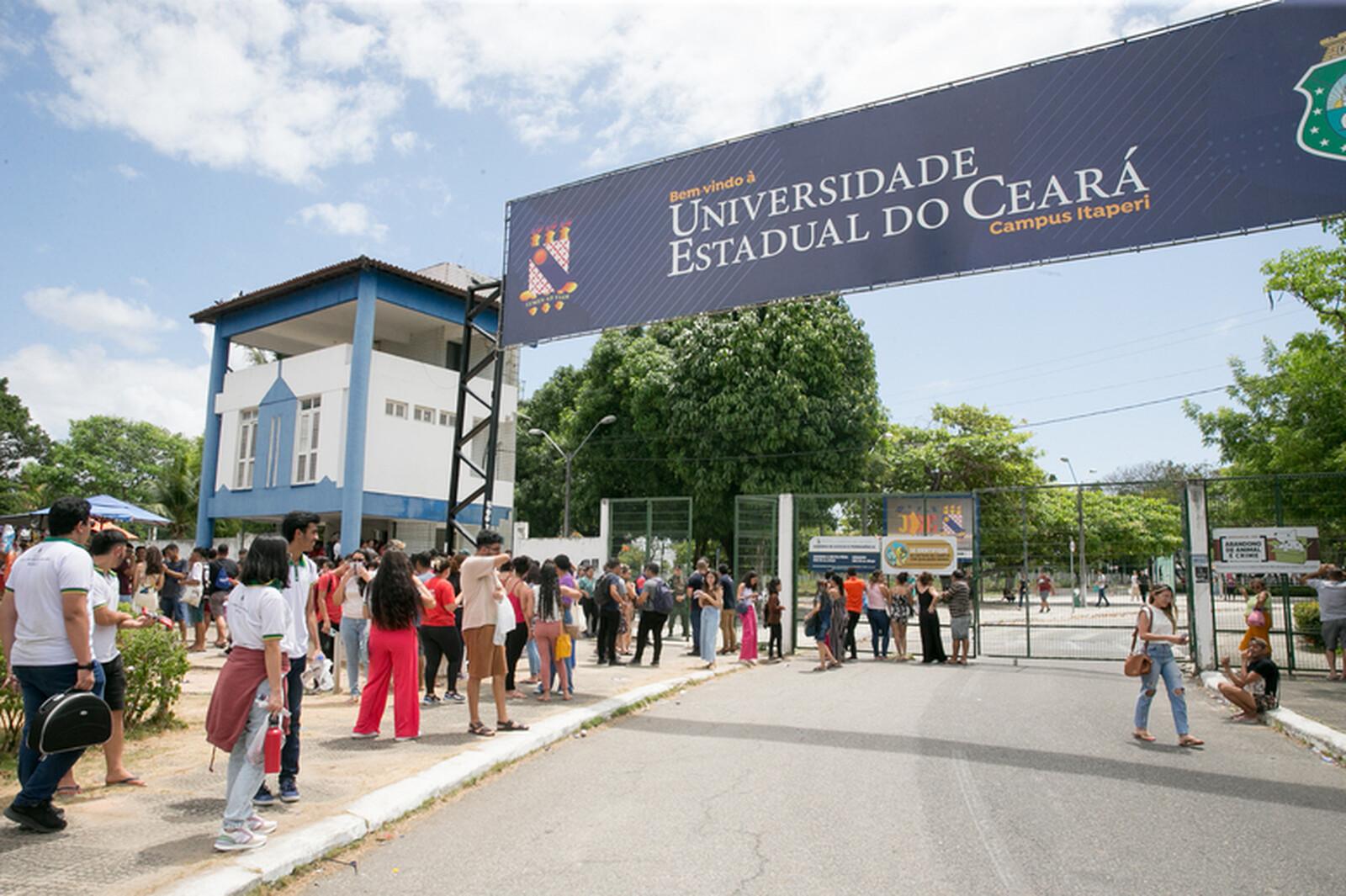 Imagem mostra fachada do campus da Uece no bairro Itaperi, em Fortaleza. Na frente, estudantes aguardam para realizar vestibular.
