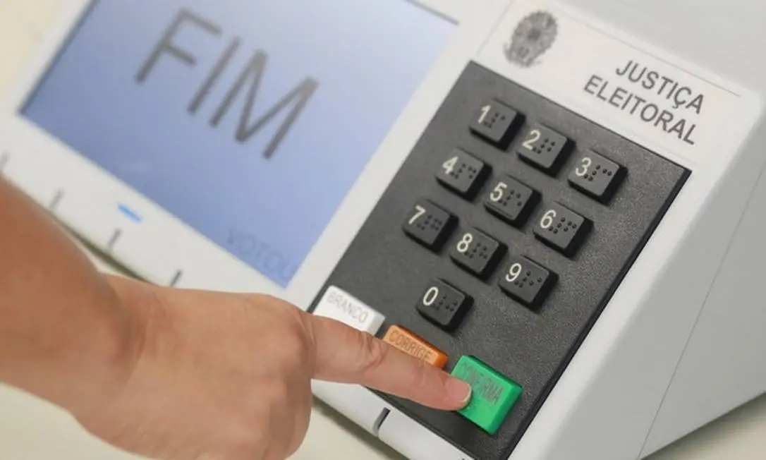 Imagem mostra uma pessoa pressionando o botão verde “CONFIRMA” em uma urna eletrônica da Justiça Eleitoral brasileira. O visor do equipamento exibe a palavra “FIM”, indicando o encerramento do voto.