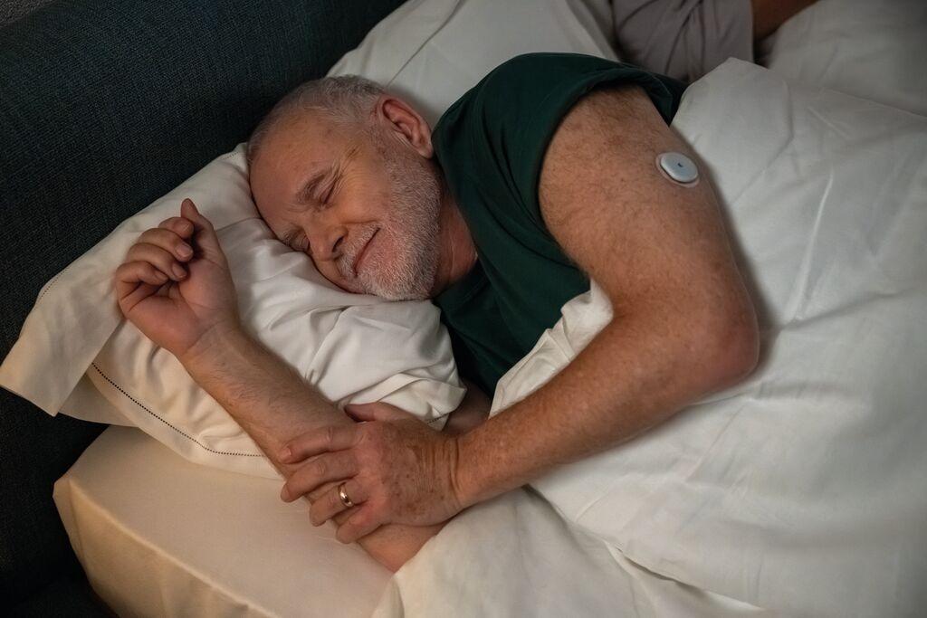 Imagem de um homem diabético dormindo com sensor no braço para matéria sobre novo sensor de glicemia usa inteligência artificial para prever quedas de açúcar.
