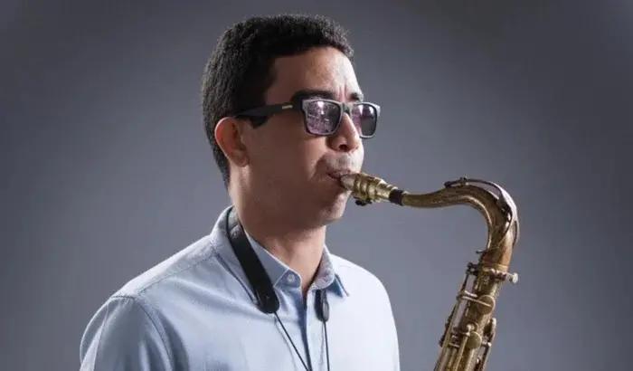 Foto do saxofonista cearense Lucas Marden, que está de óculos escuros e soprando o instrumento na imagem.