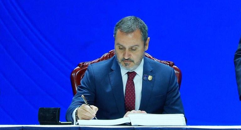 Na foto aparece o diretor-geral da Polícia Federal brasileira, Andrei Rodrigues, assinando um documento. Ele veste um terno e atrás dele tem um fundo azul.