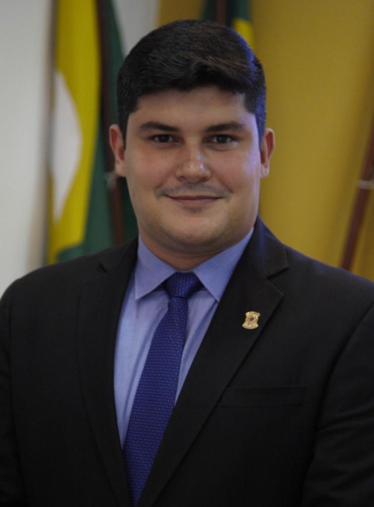 Joel Barroso é um jovem branco de cabelo preto bem cortado. Na foto, ele está com um leve bigode e usa terno preto com camisa social azul e gravata da mesma cor.