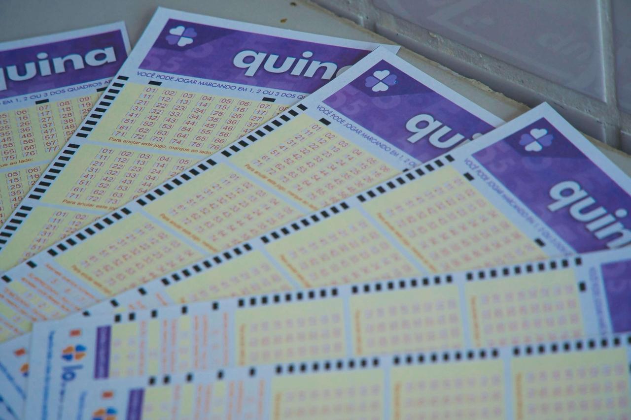 A imagem mostra vários bilhetes de loteria Quininha espalhados sobre uma mesa, com destaque para a marca no topo dos bilhetes.