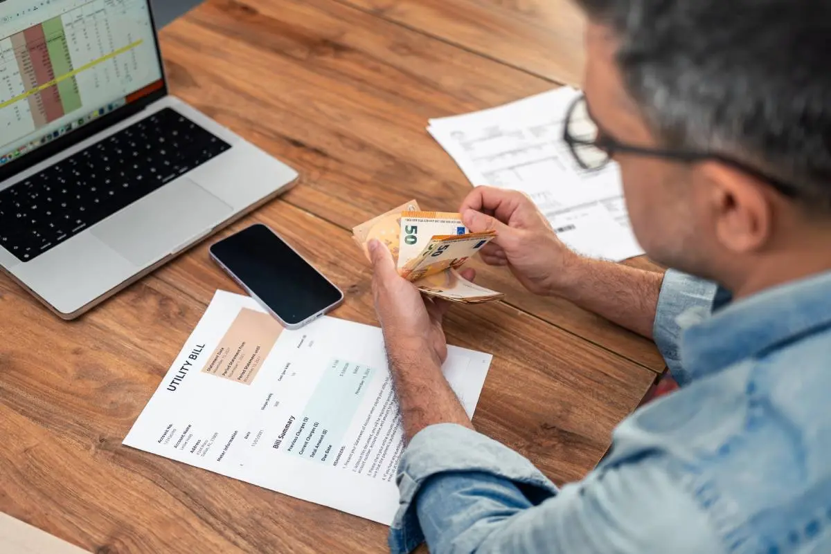 Imagem mostra home contando dinheiro e com um boleto sobre a mesa.