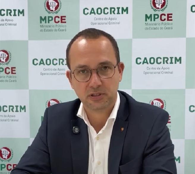 Promotor de Justiça Paulo Lima, um homem branco, de óculos e roupa social em frente a banner do MPCE.