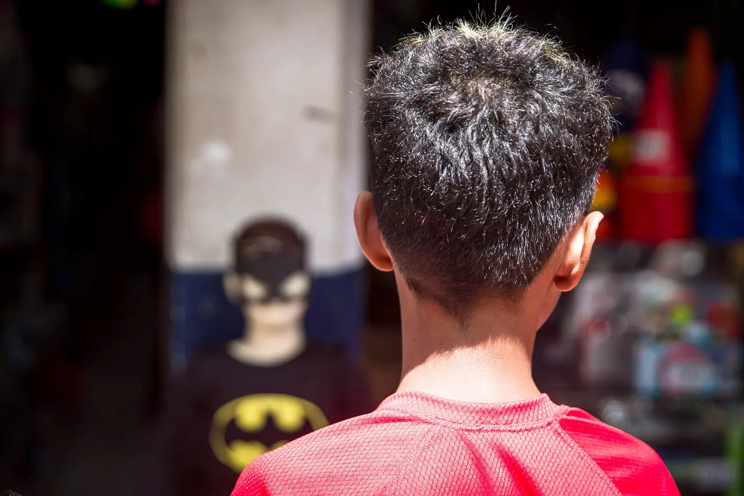 Menino de costas e blusa vermelha em frente a um manequim infantil com fantasia de Batman.