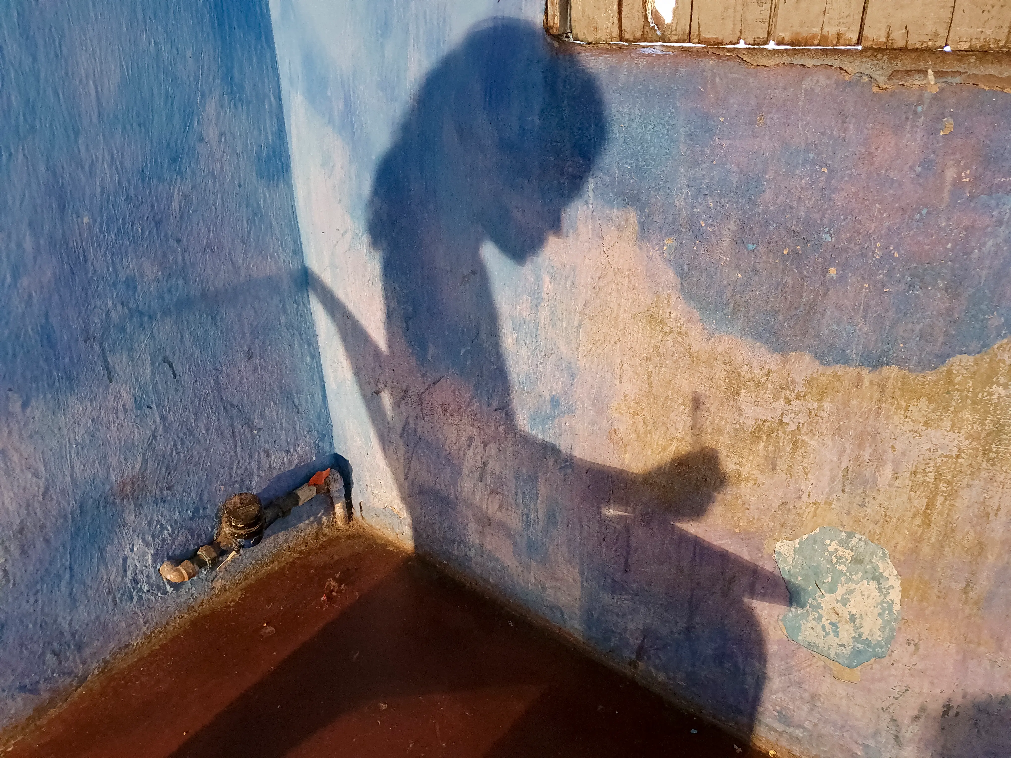 Sombra de menina sentada em cadeira refletida em uma parede azul, representando vulnerabilidade e sofrimento.