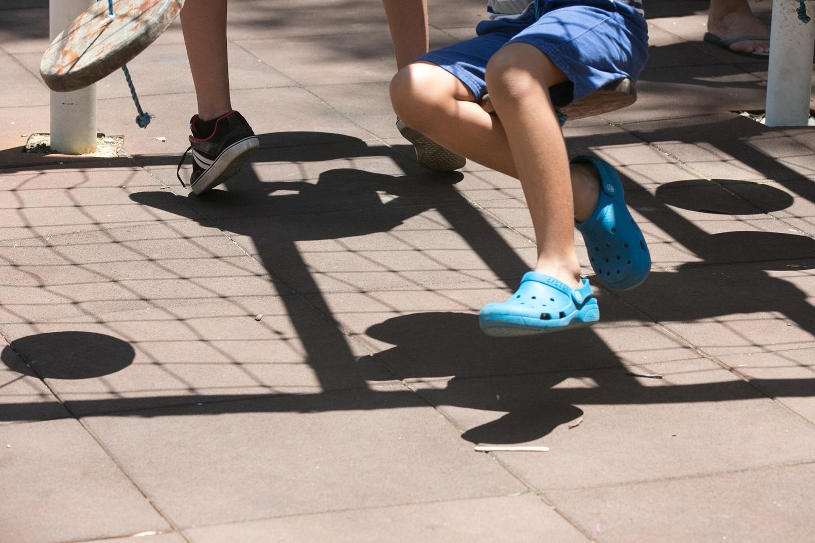 Foto detalhe das pernas de crianças brincando em balanço de parquinho.