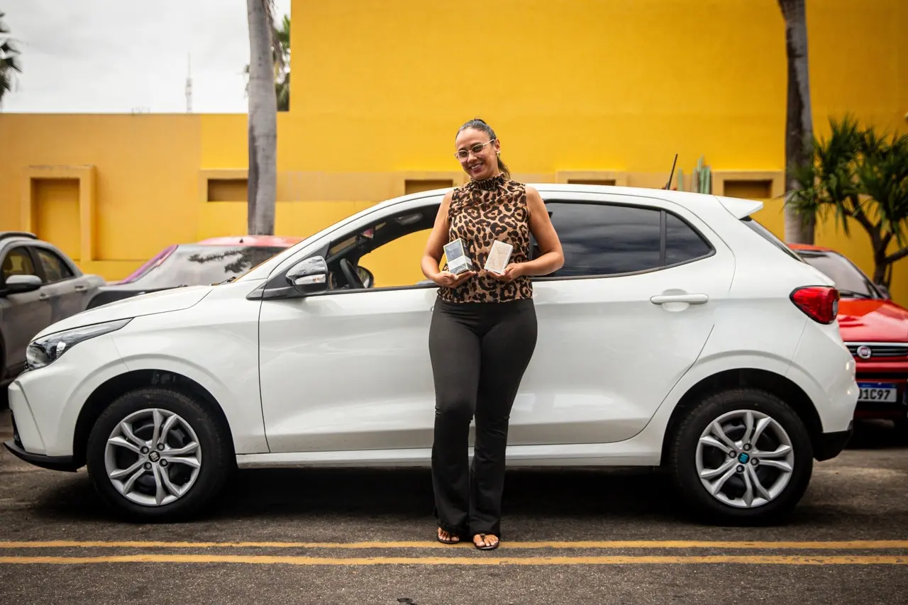 Mulher encostada em carro com produtos nas mãos.