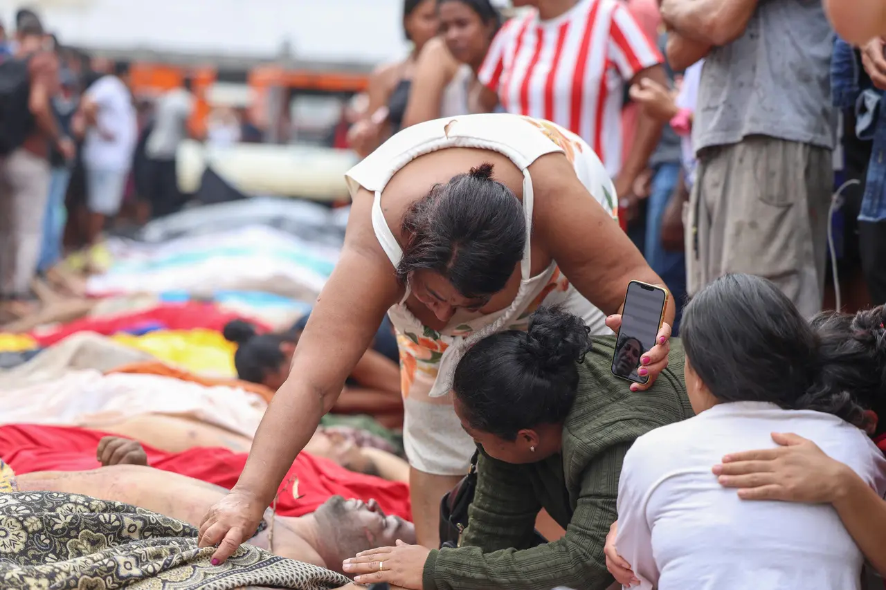 Pessoas tristes e desesperadas em um ambiente de crise, com uma mulher consolando outra e várias pessoas deitadas no chão, em uma situação de emergência ou desastre.