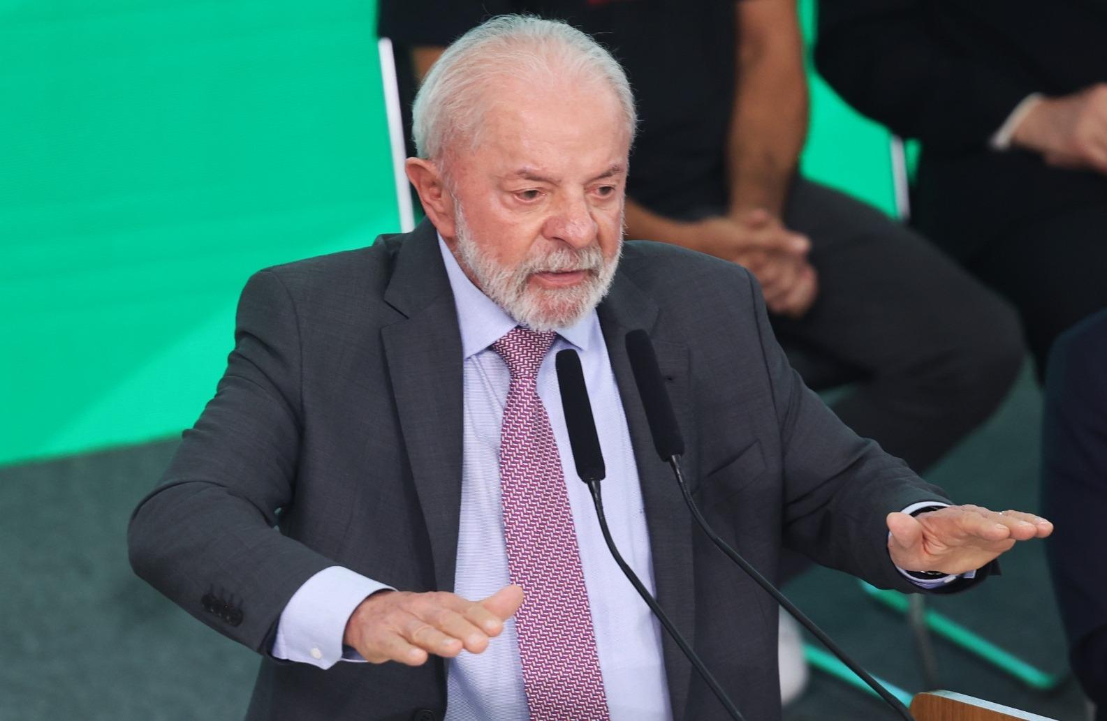 Presidente Lula gesticula durante discurso. Ele é um homem idoso, branco, de cabelos grisalhos, e, na foto, usa terno cinza, camisa social lilás e gravata da mesma cor.