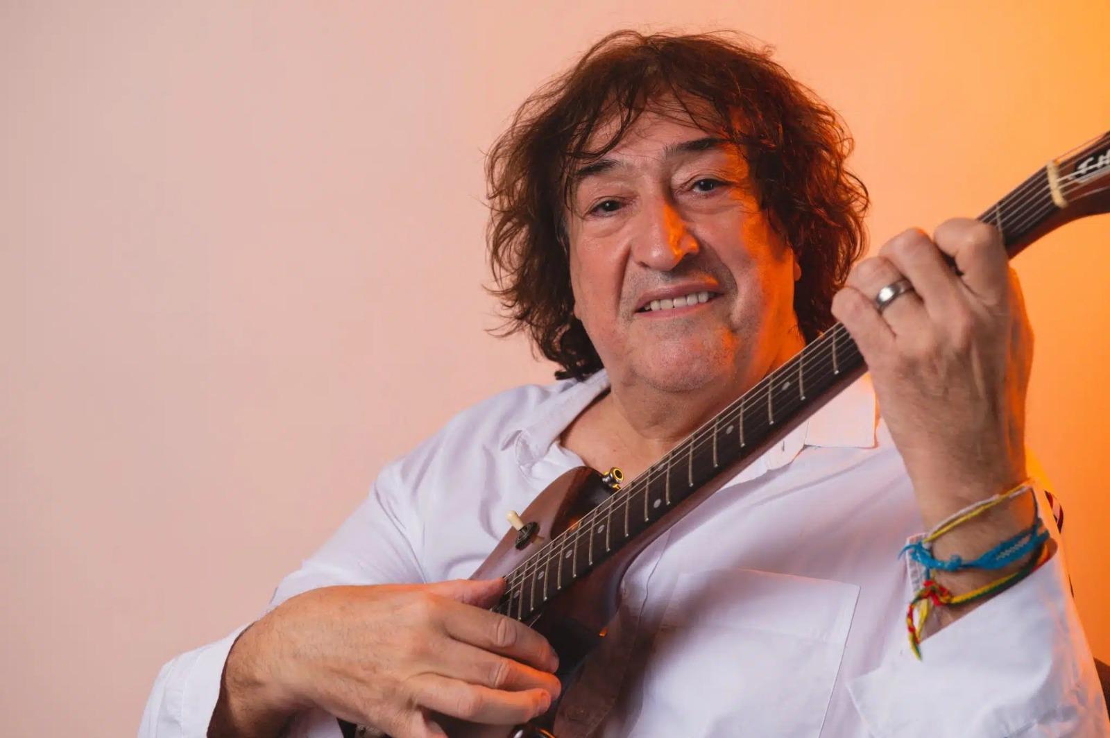 Imagem do cantor Toinho Horta toocando guitarra e sorrindo.