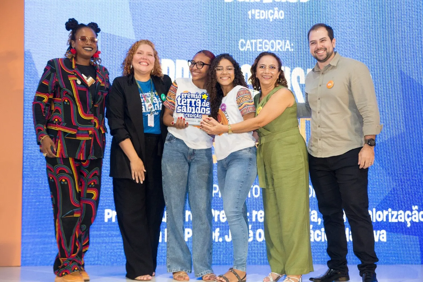 Imagem mostra seis pessoas, sendo cinco mulheres e um homem, em um palco durante entrega do Prêmio Terra de Sabidos.