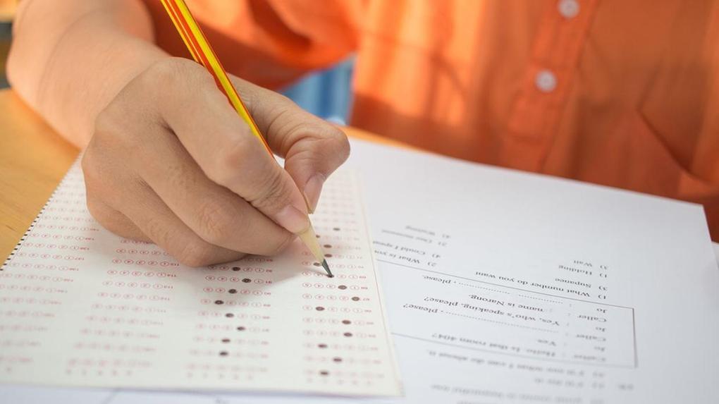 Estudante preenchendo cartão de respostas do Enem com lápis durante prova em sala de aula.