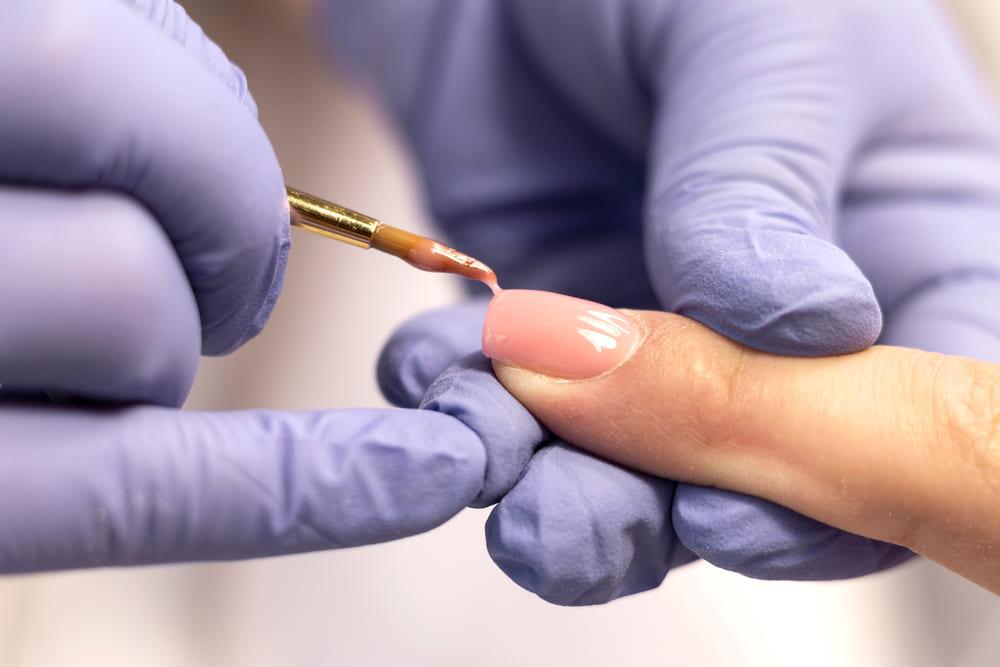 foto de profissional aplicando esmalte em gel em unha de cliente.