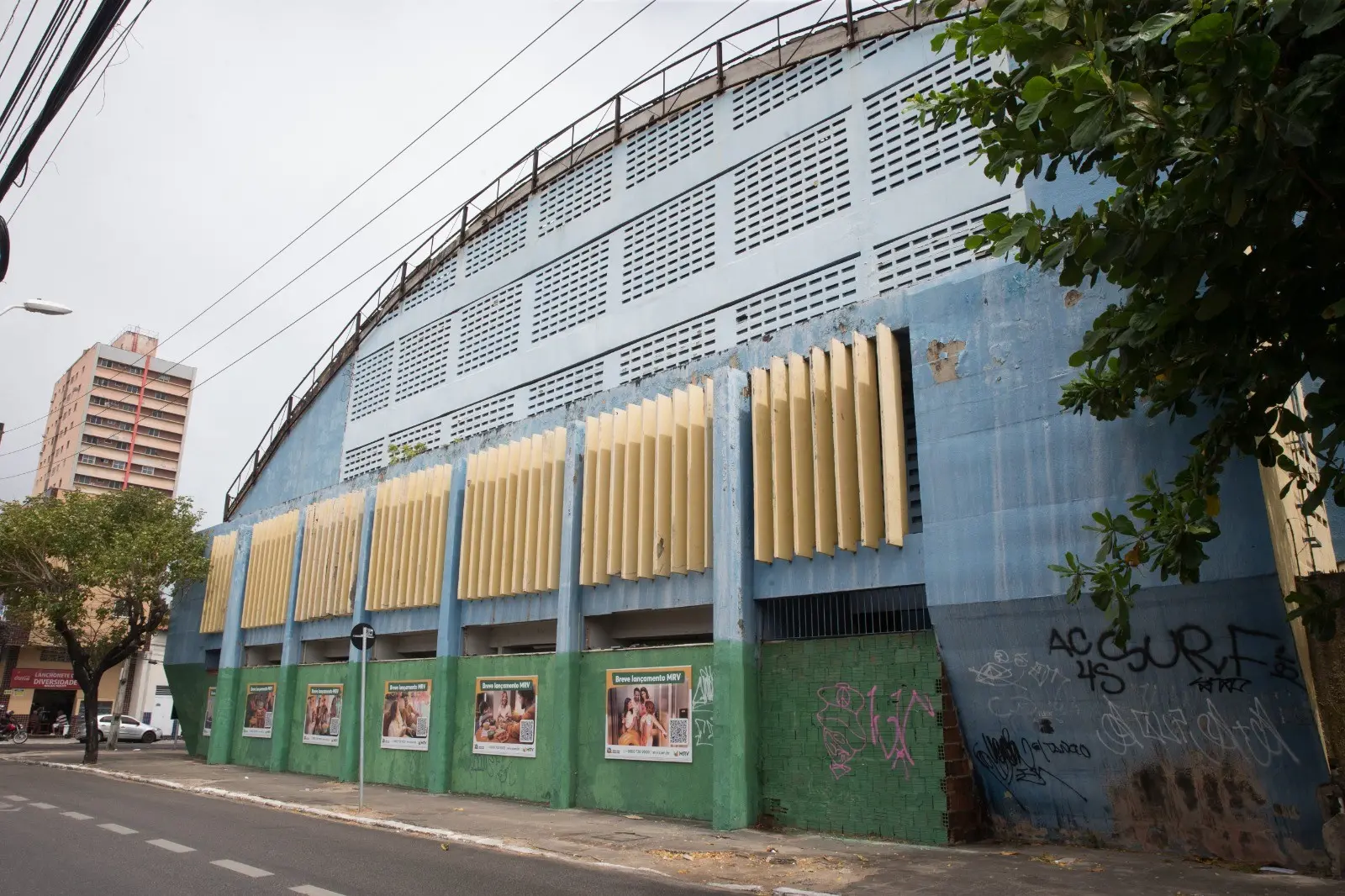 Vista lateral do ginásio do Colégio Marista, uma grande estrutura azul e verde com detalhes amarelos.