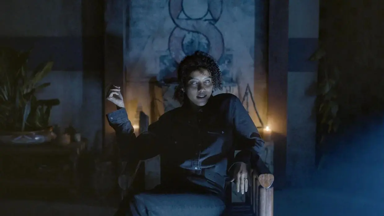 Taís Araújo olha para a câmera em um cenário escuro. Há uma luz fantasmagórica atrás dela e seus olhos estão totalmente brancos.