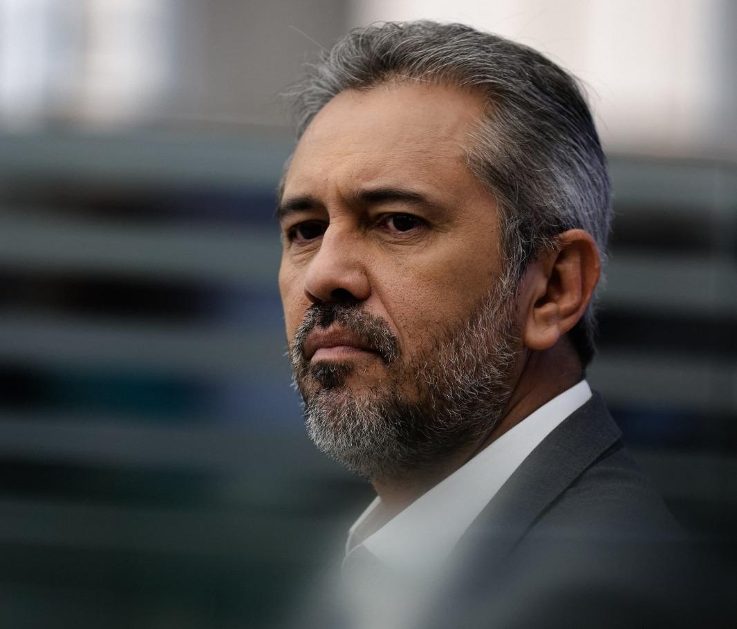 Elmano é um homem de meia idade de cabelos, bigode e barba grisalhos. Na foto, ele está sério, olhando para o lado.