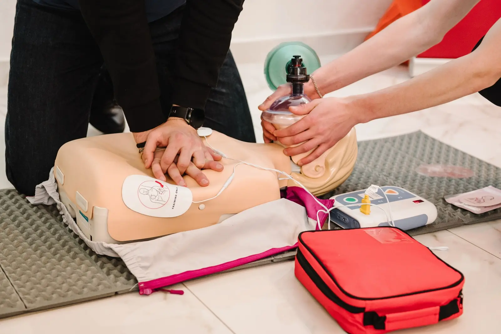 Imagem mostra simulação de reanimação cardíaca com desfibrilador automático externo em boneco de borracha.