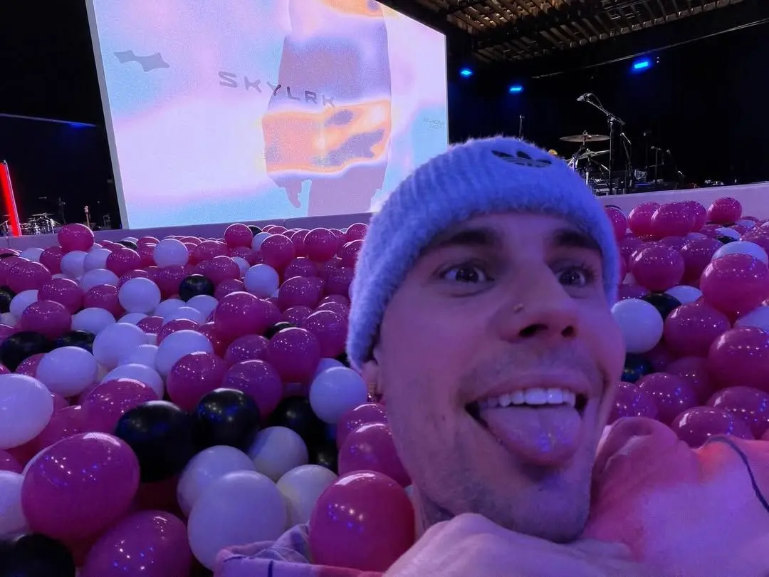 Justin Bieber em uma piscina de bolinha, aparecendo só sua cabeça com um telão ao fundo.