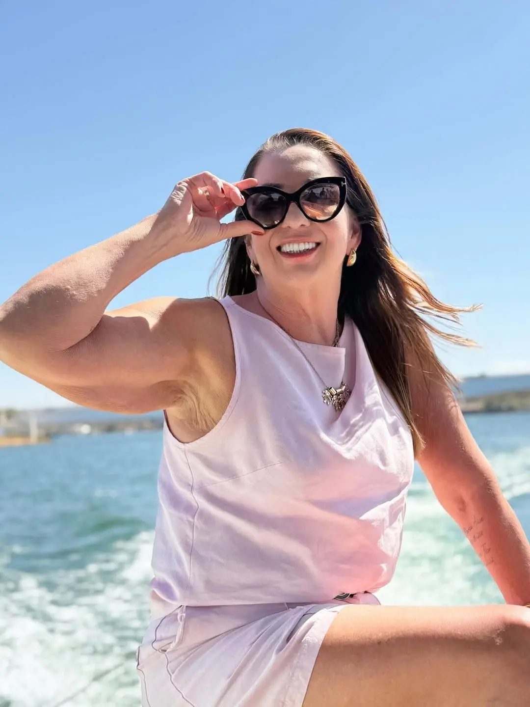 Margareth Serrão de óculos escuro, vestido branco e posando na praia.